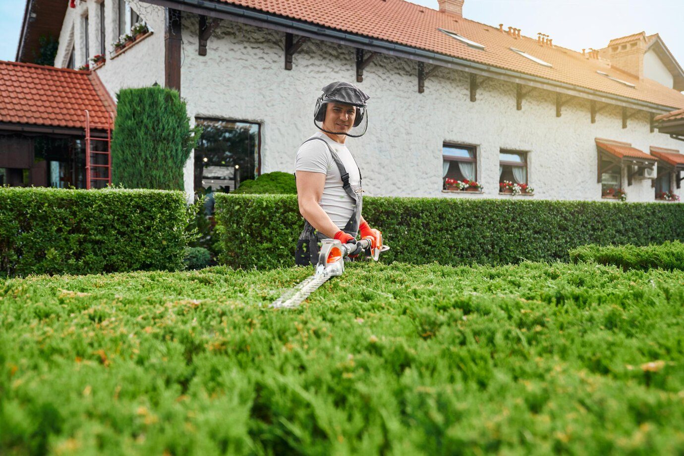Man in uniform glasses and gloves pruning bushes at garden
